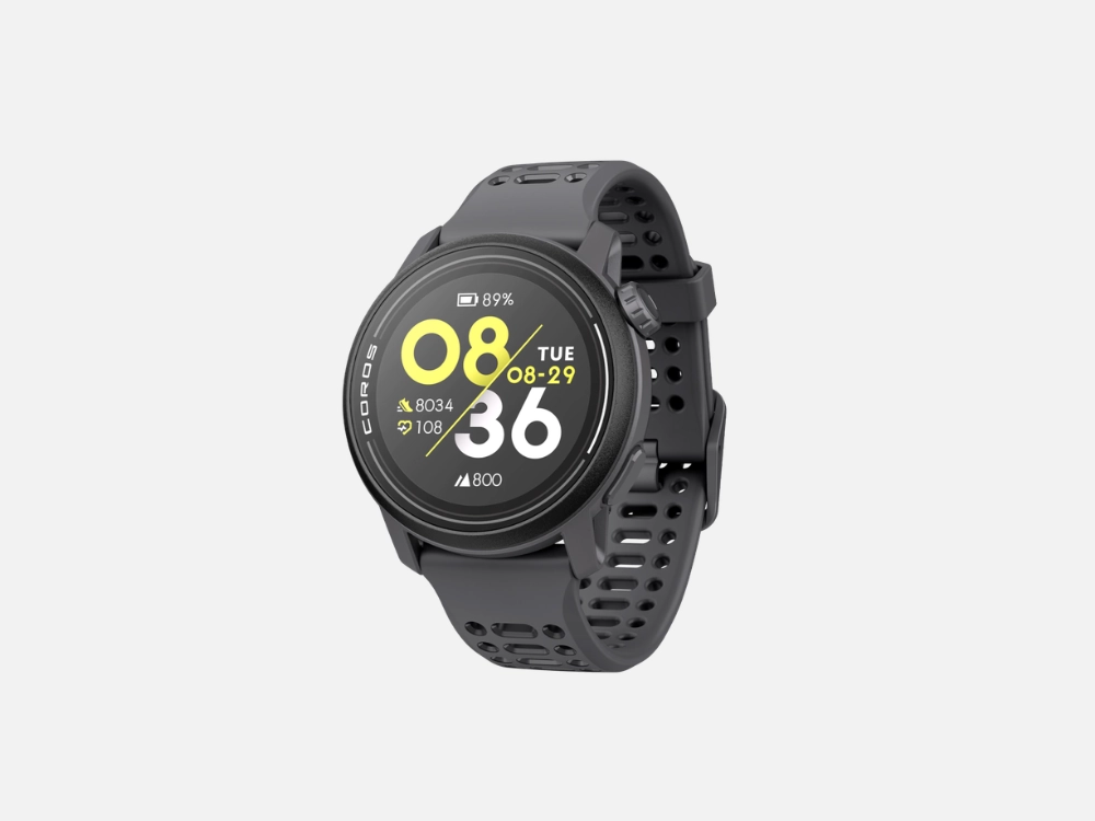 Imagem em fundo cinza de um Coros Pace 3 preto, um smartwatch para corrida de alta performance. O visor circular exibe a hora digital '08:36', o nível de bateria '100%', e métricas de passos (8043) e queima de calorias (650), além da data 'TUE 29' e do horário do pôr do sol (18:55). A palavra 'COROS' está visível no mostrador. O relógio possui uma pulseira de silicone preta perfurada.