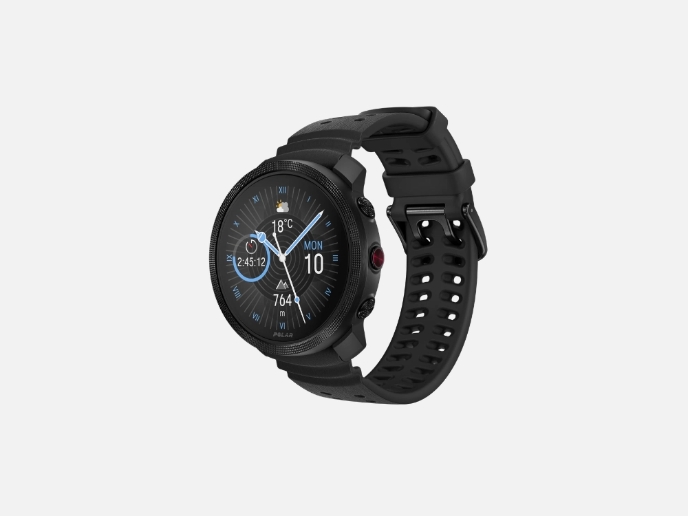 Imagem em fundo cinza do Polar Vantage M3 na cor preta. Este smartwatch para corrida possui um mostrador digital exibindo a hora "12:48", a data "MON 5", temperatura de 25°C e os horários do nascer e pôr do sol, acompanhado por um bisel texturizado e pulseira escura.