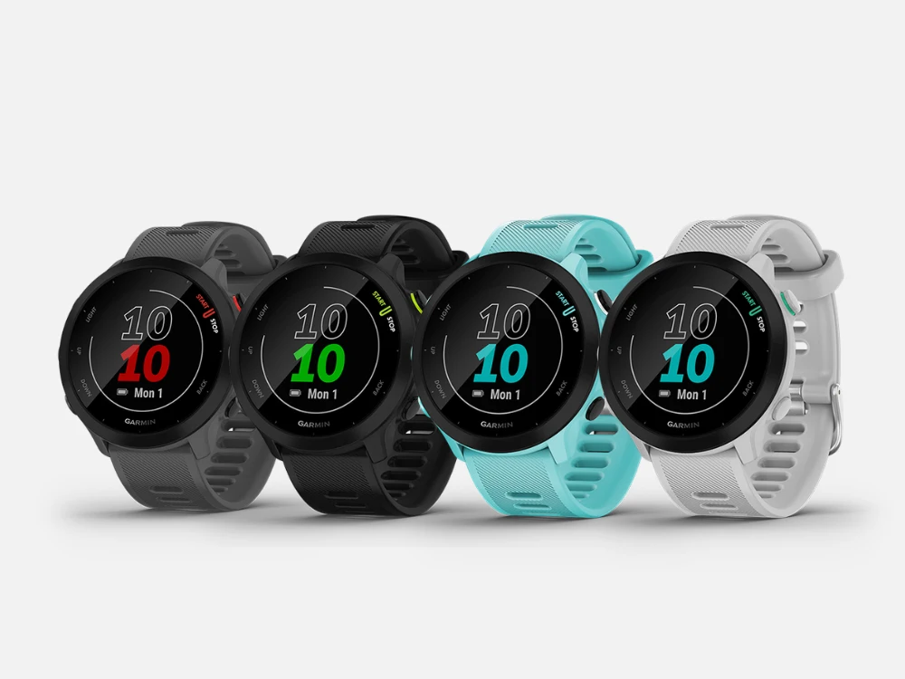 Quatro smartwatches da marca Garmin enfileirados lado a lado sobre um fundo claro. Da esquerda para a direita, as pulseiras são nas cores cinza, preto, azul-claro e branco. Todos os relógios possuem a tela digital redonda ligada, exibindo a hora 10:10.