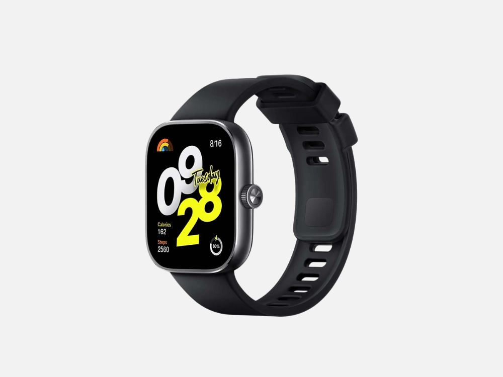 Fotografia de um smartwatch preto com tela quadrada e cantos arredondados, posicionado em ângulo sobre um fundo cinza claro. A tela exibe o horário "09:28" em grandes algarismos brancos e amarelos, junto com a data "8/16 Tuesday", um ícone de arco-íris, queima de calorias (162), contagem de passos (2560) e nível de bateria (80%). O relógio possui um botão lateral de metal e uma pulseira de silicone preta texturizada com fivela preta.